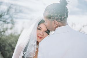 Intimate outdoor wedding portrait of couple embracing with sunlight creating a dreamy glow through bridal veil.