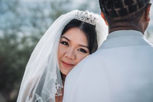 Bride wearing delicate tiara and veil smiles radiantly during outdoor wedding photoshoot.