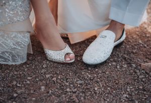 Wedding shoes detail shot showing bride's sparkly heels next to groom's white loafers.