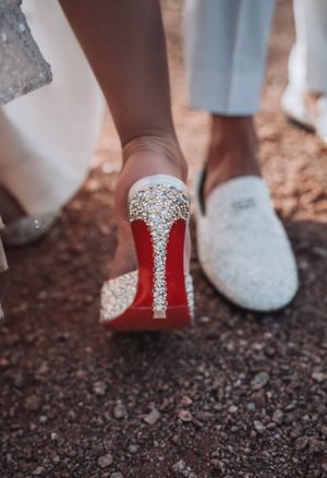 Close-up of red-soled bridal shoes with crystal embellishments on desert ground.