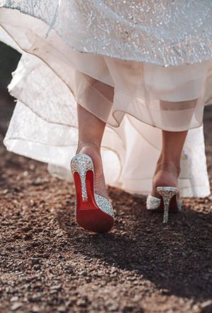 Elegant bridal shoes with crystal details and red soles captured against desert terrain.