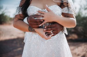 Wedding detail shot showing hands with rings intertwined against sparkly white dress.