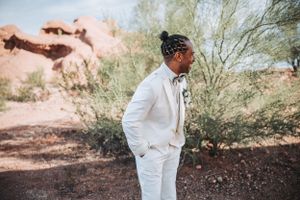 Wedding photography in a desert setting shows a classic white tuxedo with bowtie against rustic red rock formations.