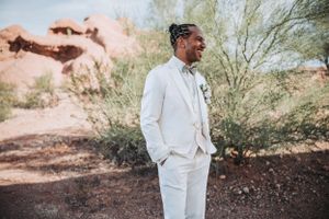 Desert wedding photography with someone in an elegant white suit posed against natural rock formations and desert flora.