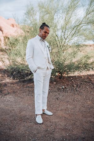 A desert wedding portrait showcases a complete white ensemble from suit to shoes against a rugged natural backdrop.