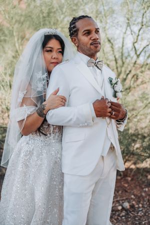 A romantic wedding portrait features a bride in sparkles and veil with groom in white against desert scenery.
