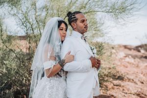 Desert wedding photography captures a couple in traditional white attire against rocky terrain and sparse vegetation.