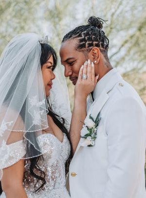 Intimate wedding portrait showing tender moment between newlyweds in white attire against natural backdrop.