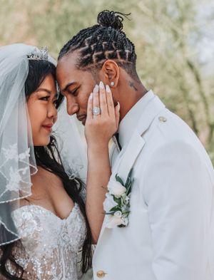 Close-up of romantic wedding moment with bride in lace dress and groom in white suit touching foreheads.