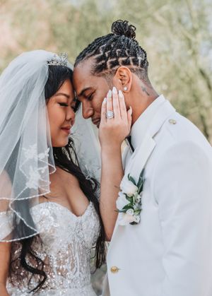 Tender wedding photo capturing intimate moment between bride in veil and groom in white jacket.