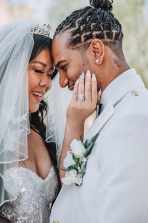 Joyful wedding portrait showing happy couple in white attire sharing intimate moment outdoors.