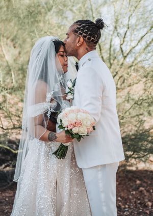 Romantic outdoor wedding photo with couple in white sharing tender moment with bouquet.