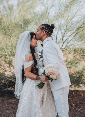 A romantic wedding couple embraces in a desert garden setting while holding a pastel bouquet.