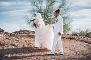 Wedding couple walking together on desert trail with bride's dress flowing in the wind.