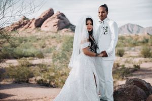 Desert wedding portrait featuring couple in white attire against mountain backdrop.
