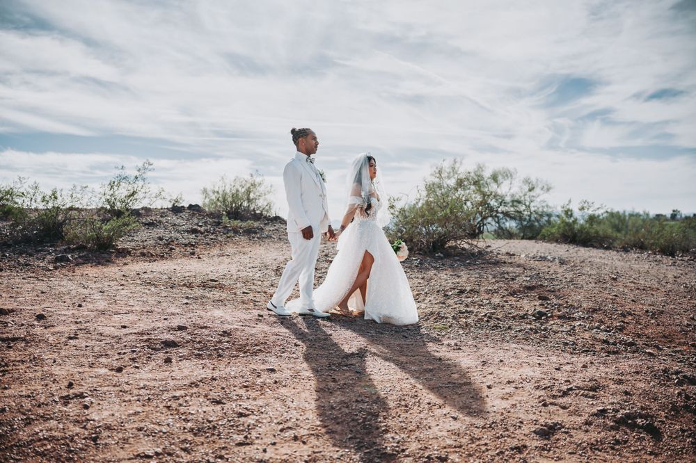 A wedding couple walks through a desert landscape under cloudy skies.
