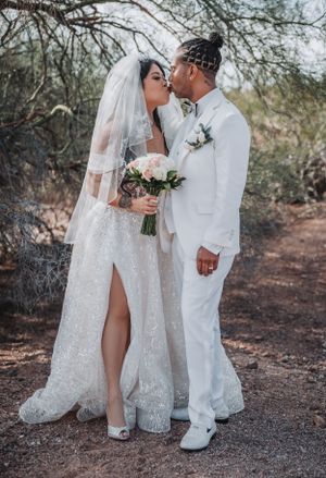 A romantic wedding portrait of a couple in white attire with a bouquet of pink roses.
