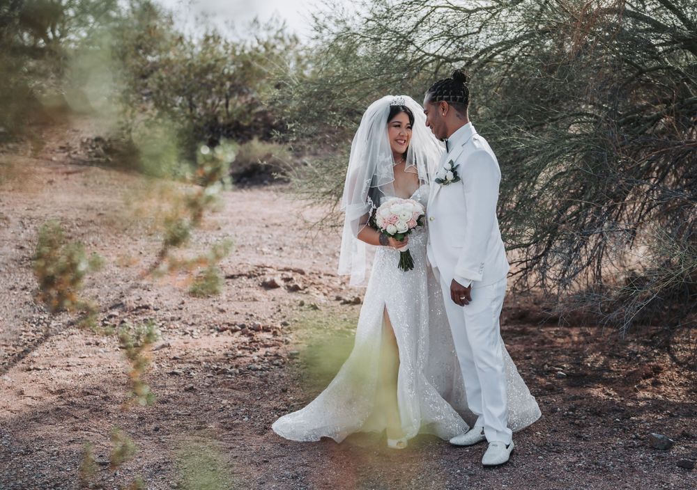 A wedding couple in white outfits share an intimate moment on a desert path.