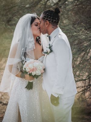 A tender moment between newlyweds with a bouquet of pink roses in a desert setting.