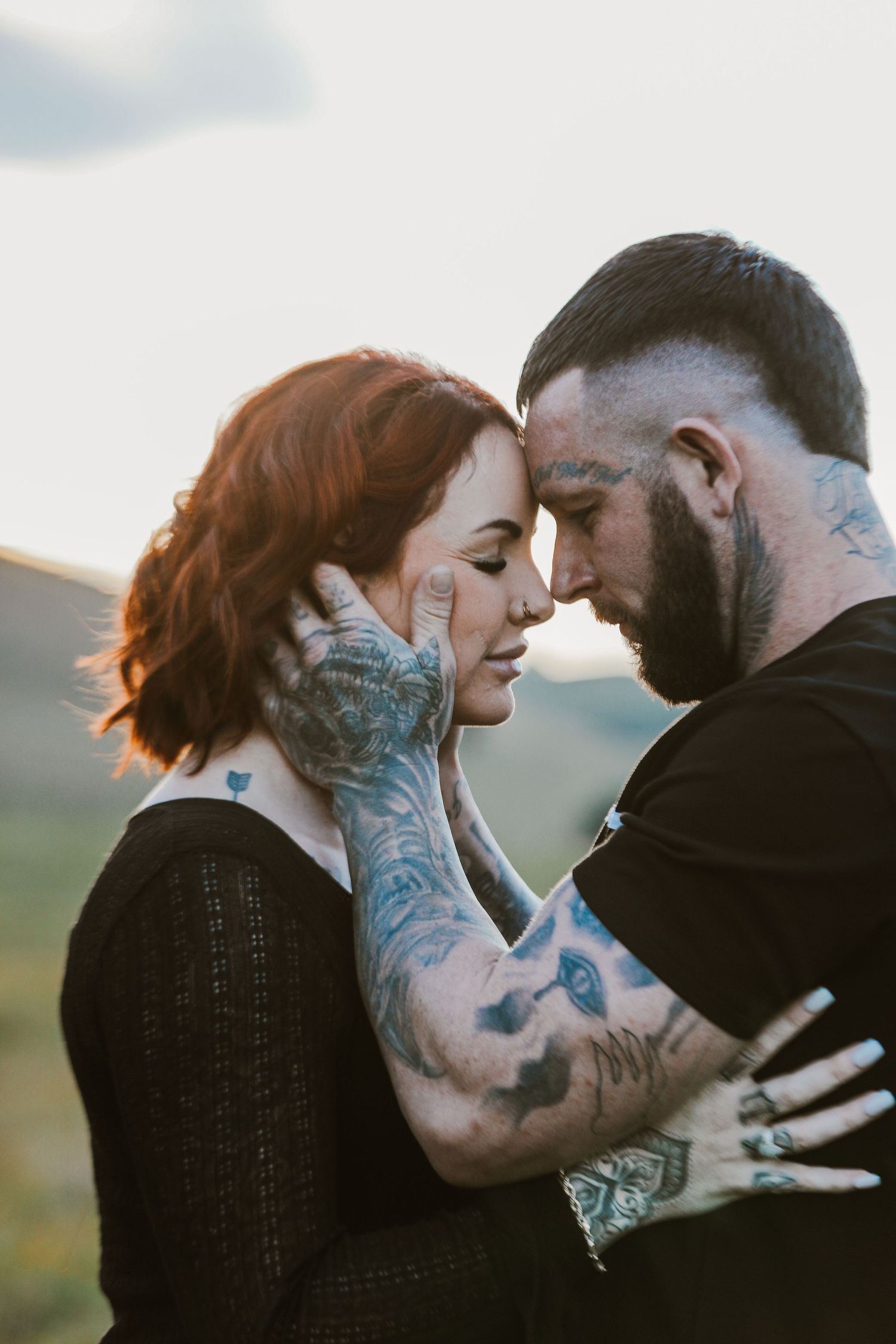 Intimate couple with tattoos sharing tender moment at golden hour.