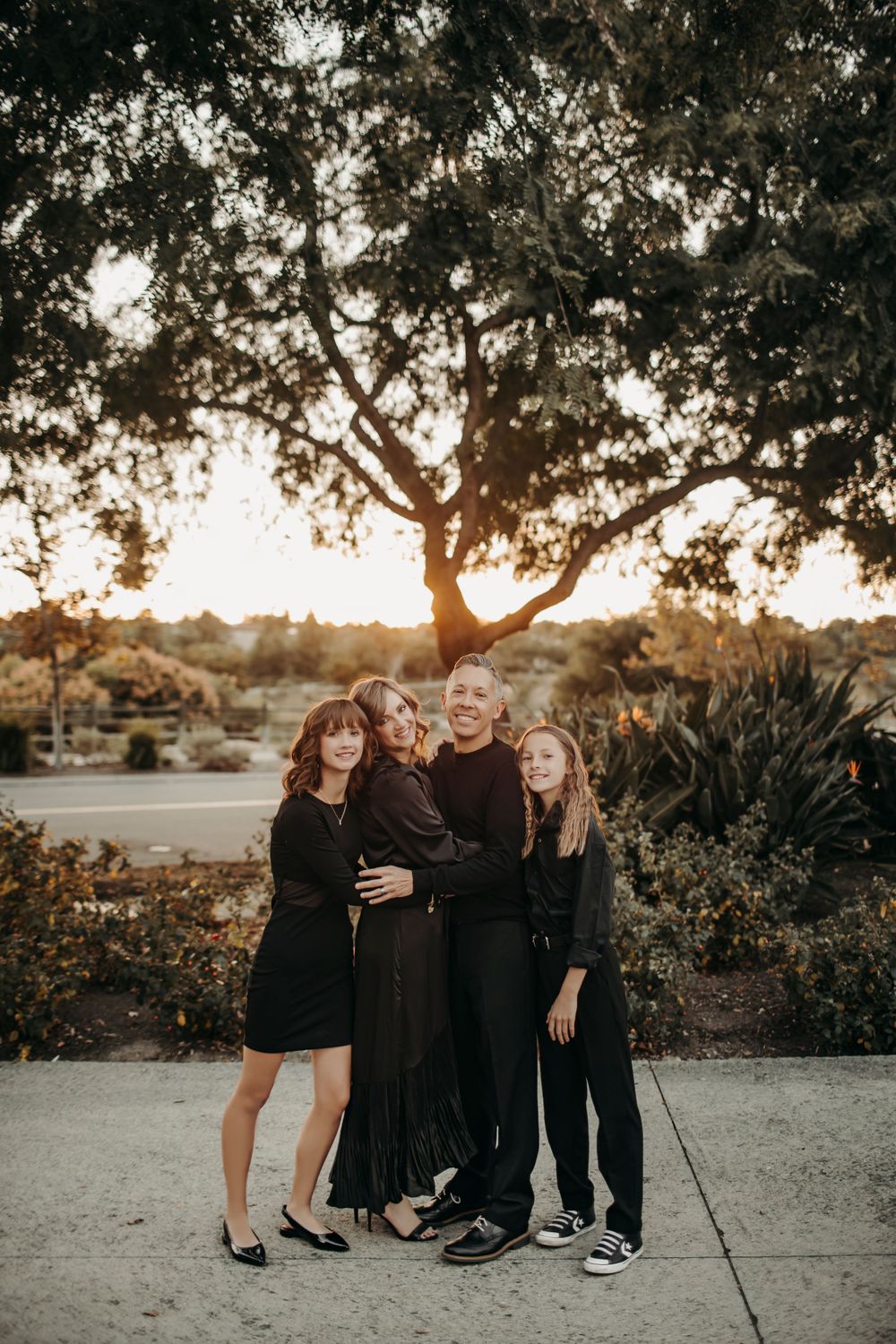 A family of four in elegant outfits posing at a country club, smiling warmly, with manicured lawns and a grand building in the background.