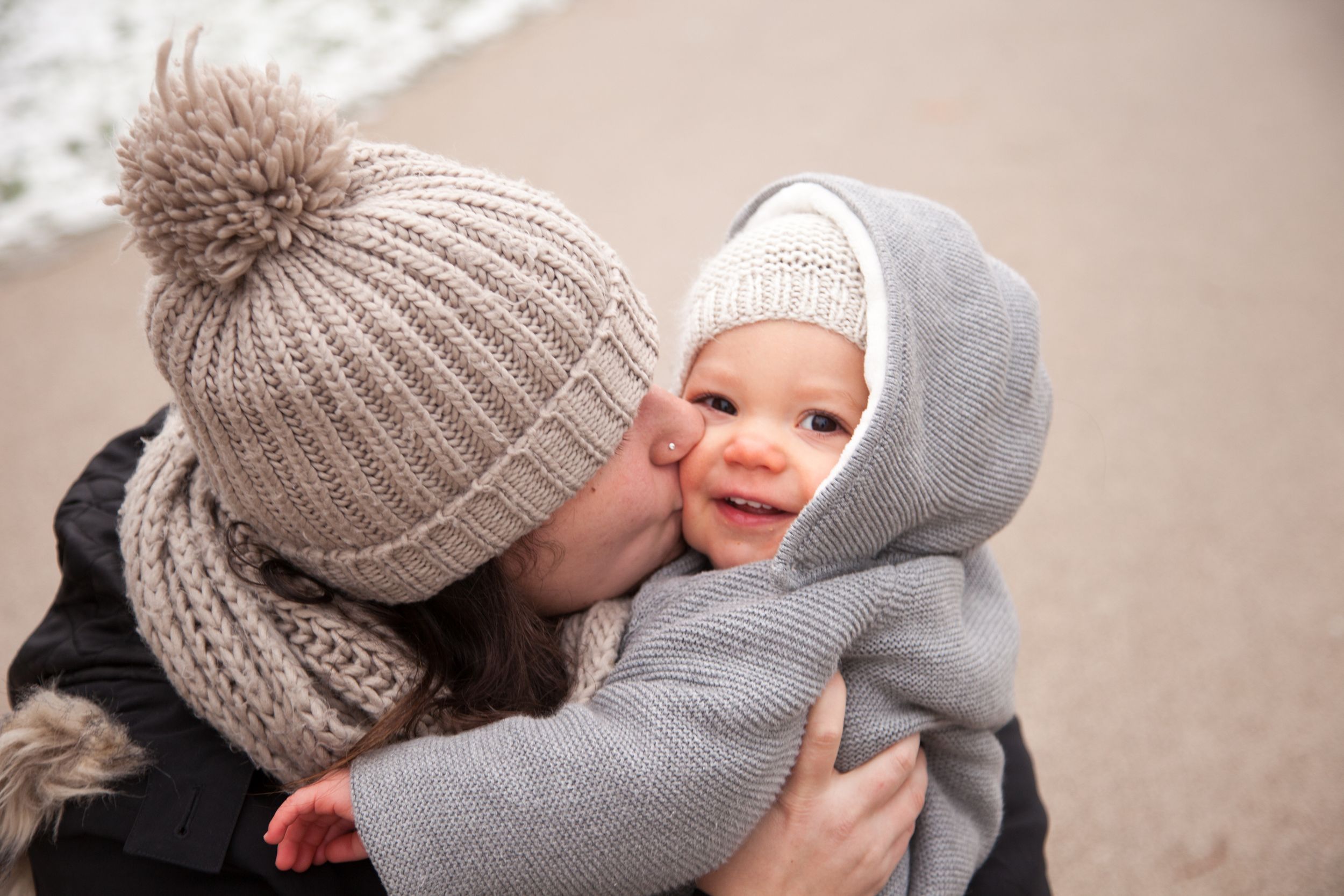 Une maman chaudement habillé pour une séance photo en hiver embrasse son bébé sur la joue.