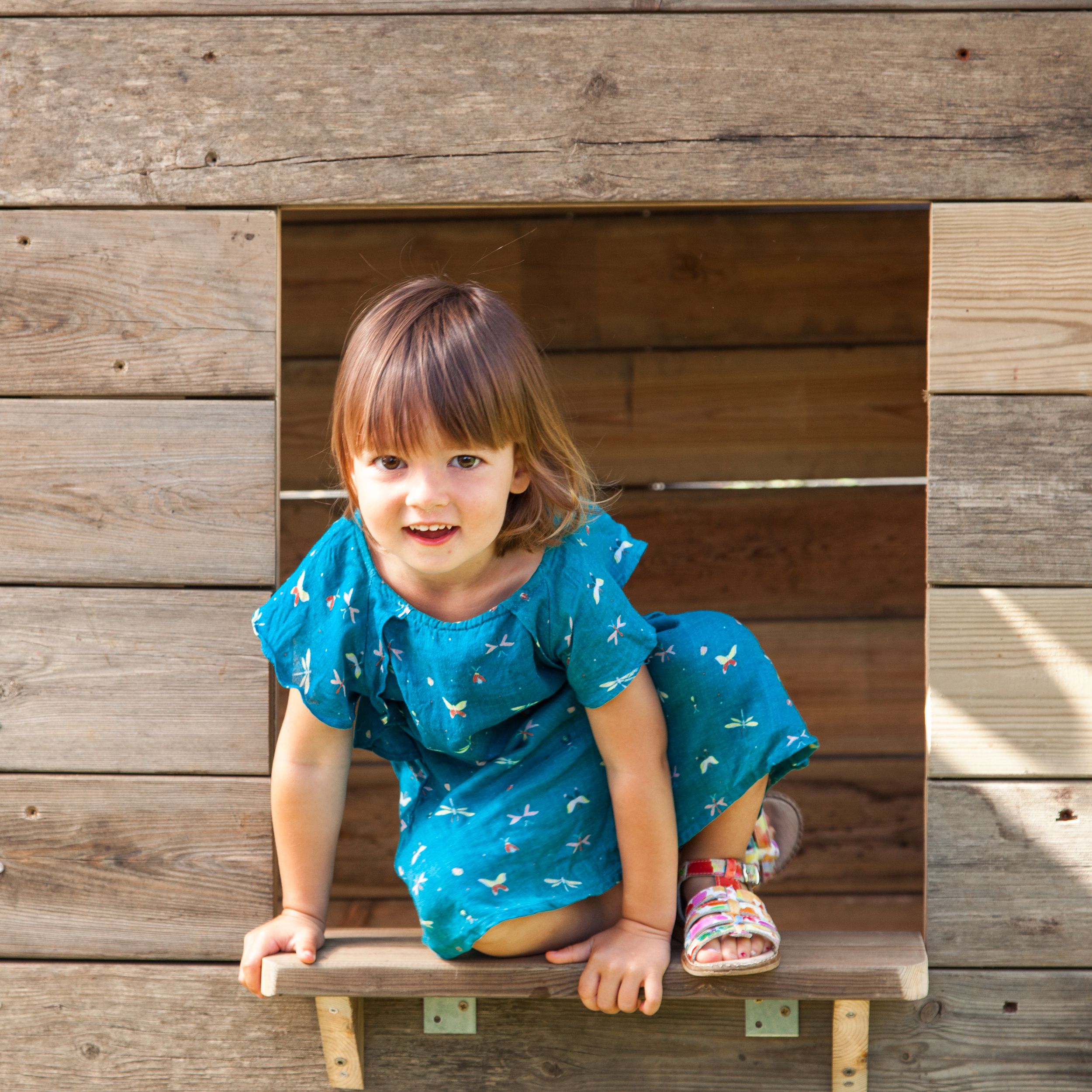 Une petite fille joue à la fenêtre de sa cabane de jardin.