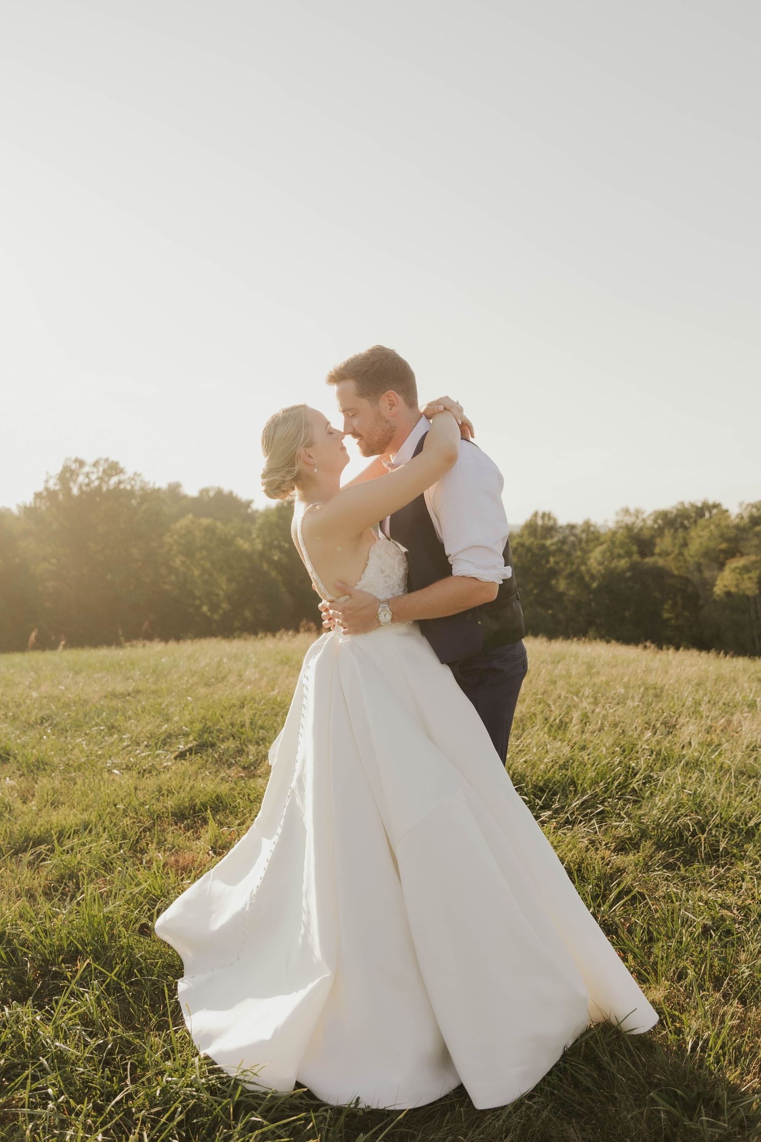 Romantic wedding couple dancing in a golden sunlit field.