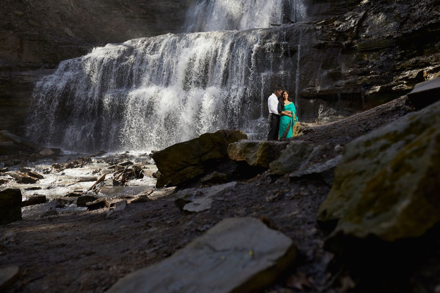 Dramatic waterfall cascading down dark rocky cliffs with tiny figures visible in distance.