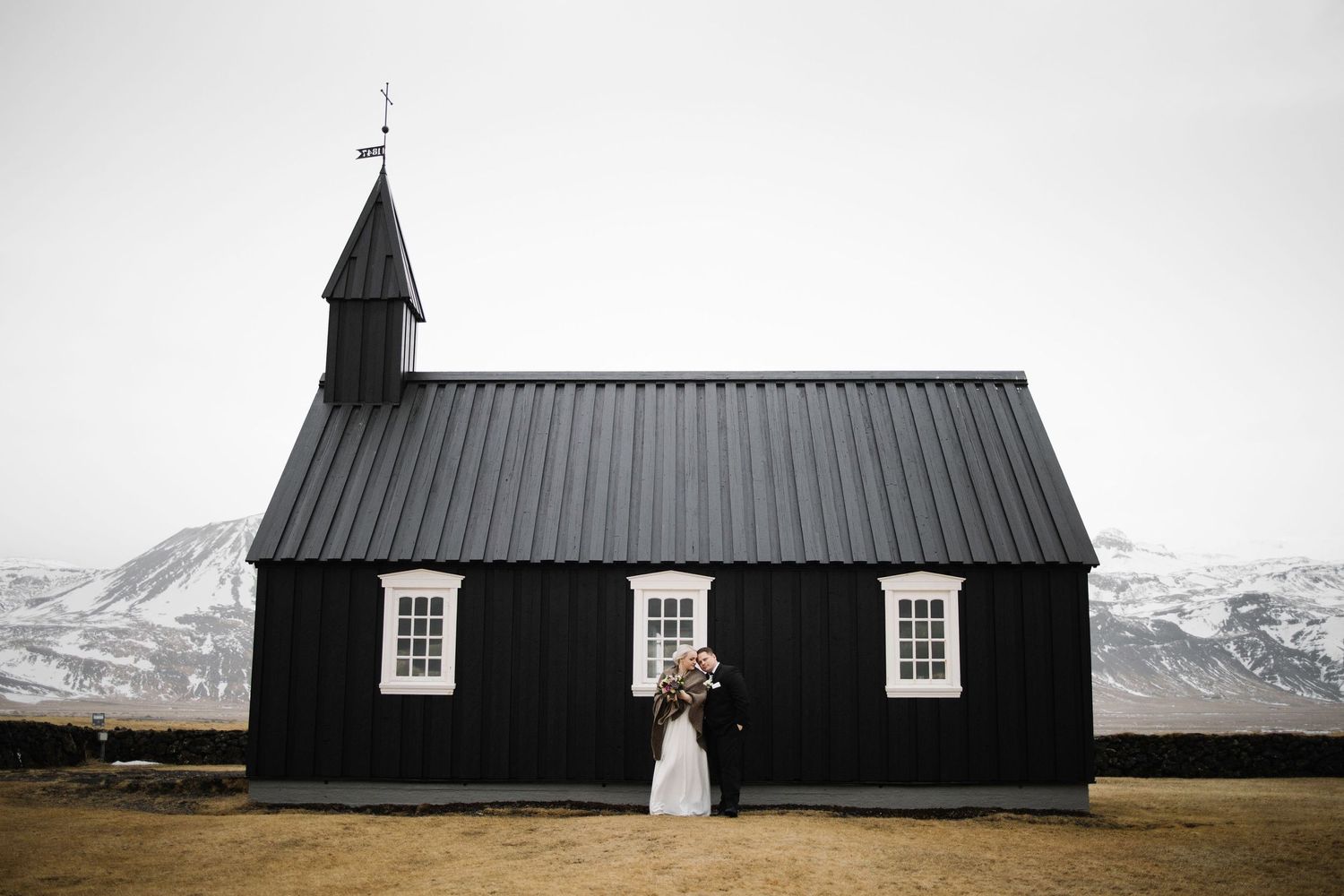 Dramatic black church building with white windows against snowy mountain backdrop.