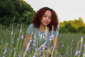 Person with curly hair sits among blooming lavender flowers in a meadow.