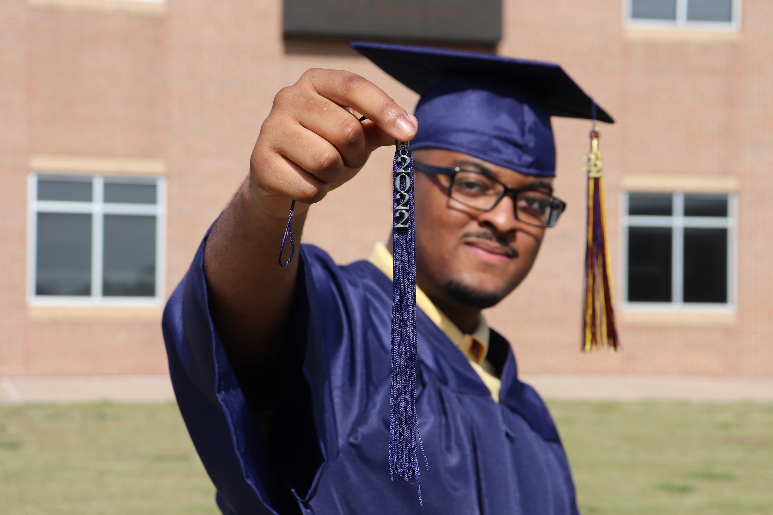 Graduate in blue cap and gown holds tassel during outdoor graduation photo.