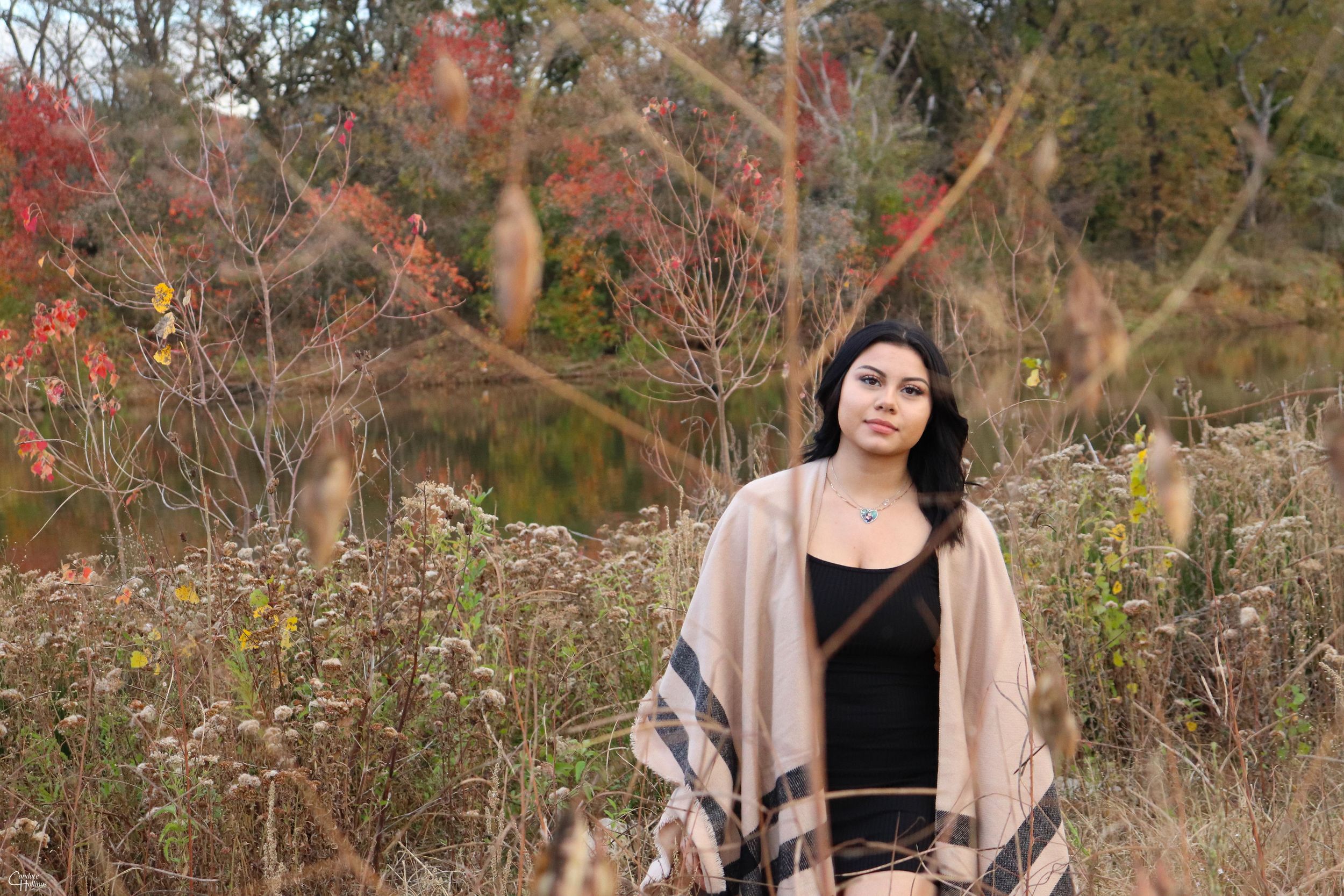 Person in beige cardigan and black top poses in autumn field.