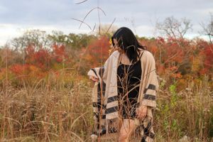 Person wearing striped cardigan stands in fall field with dried plants.