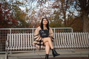 Person in cardigan and boots sits on white bench during autumn.