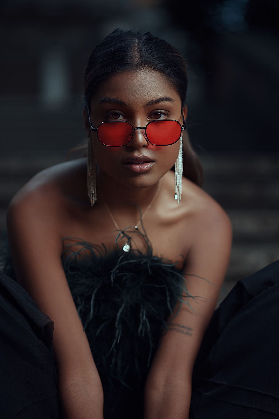 Fashion portrait with red tinted sunglasses and feathered black outfit.