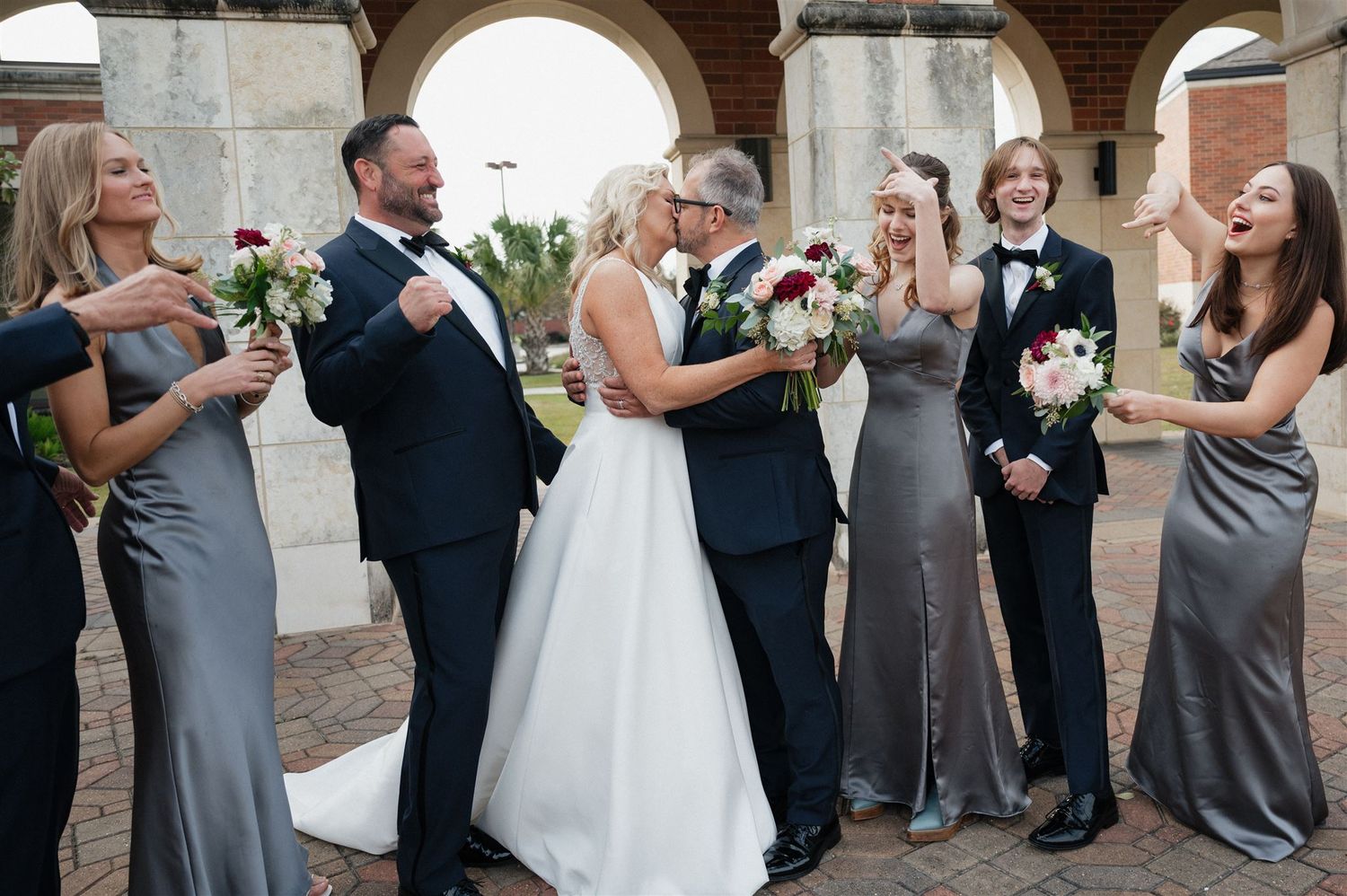 Wedding party celebrates with laughter under elegant stone archways.