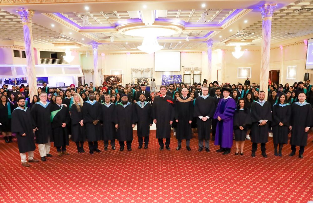 A large group gathered in a grand ballroom with ornate ceiling and purple accent lighting.