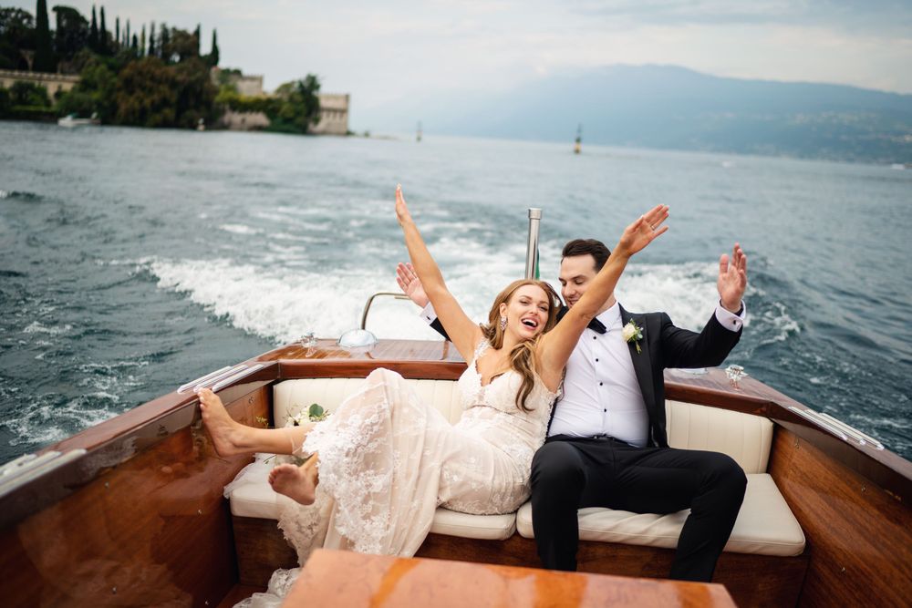 Happy couple relaxing on wooden boat while celebrating their wedding on scenic lake.