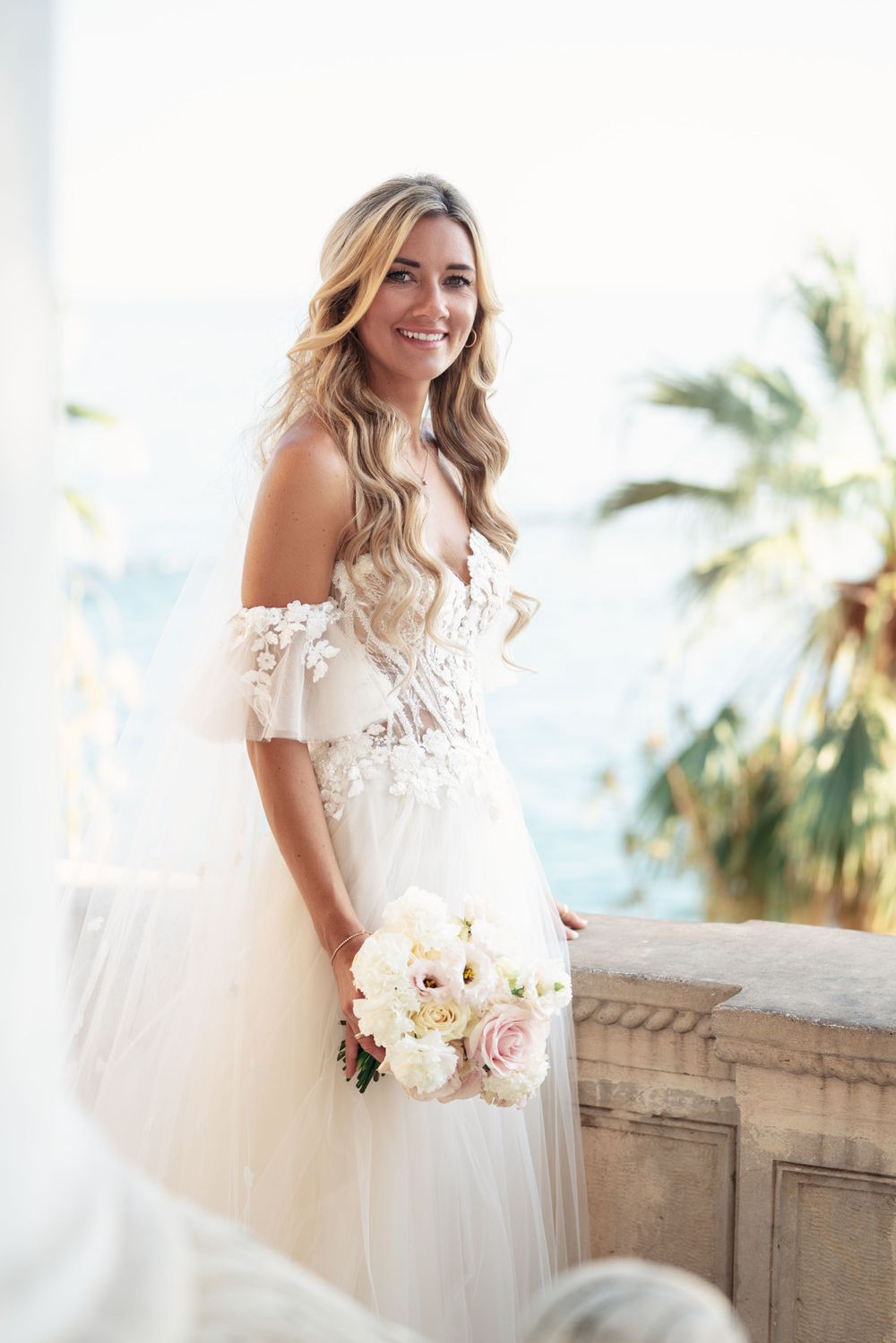 Bridal portrait on balcony featuring off-shoulder lace gown and romantic bouquet.