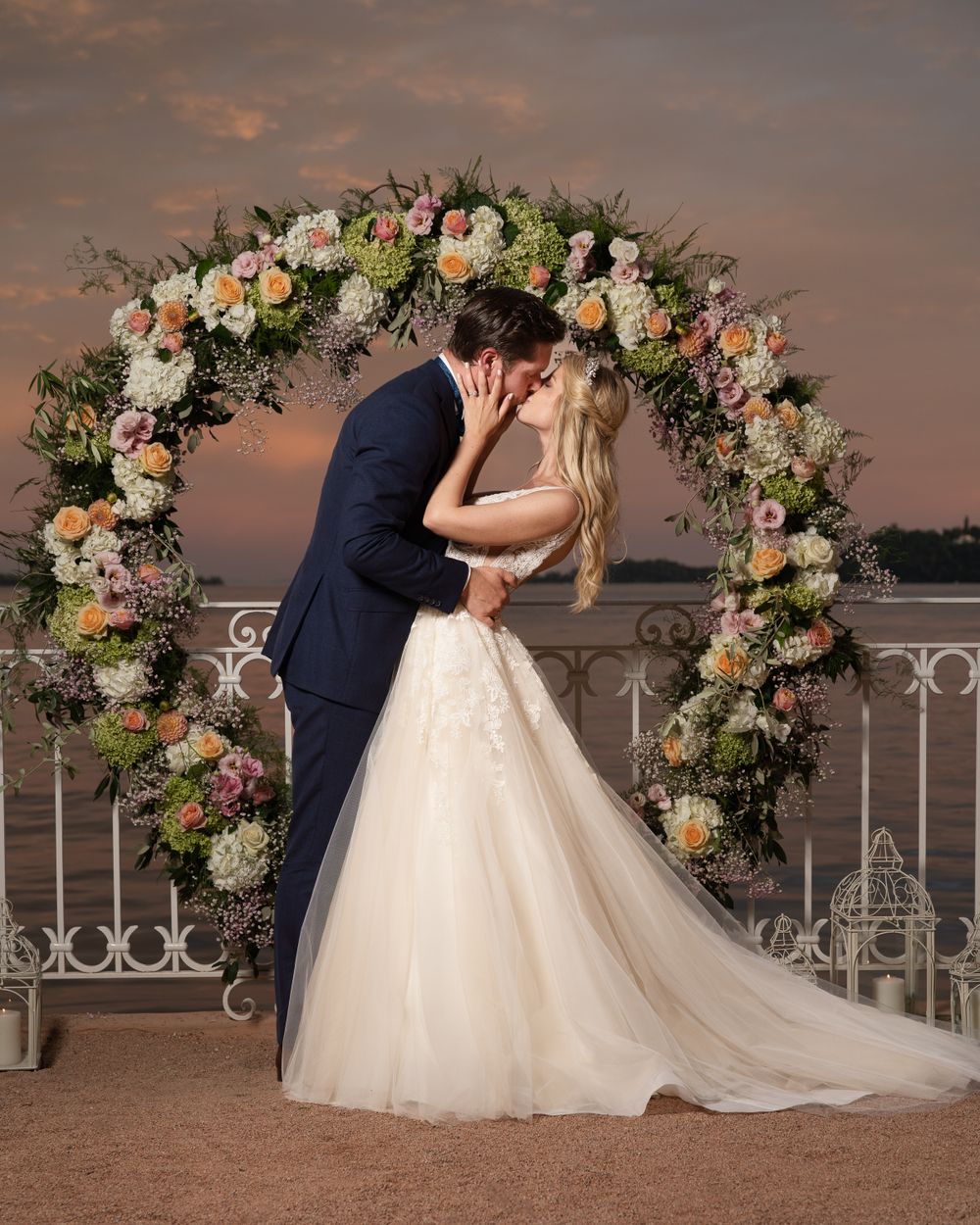 Romantic sunset wedding photos under a floral arch with peach and white blooms.