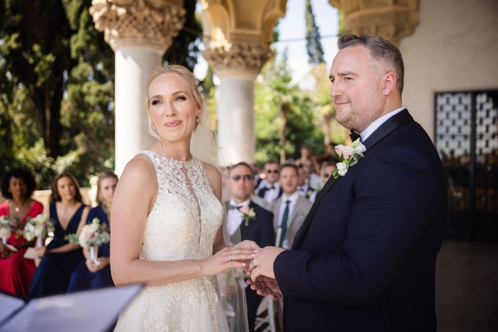Elegant outdoor wedding ceremony under stone archways with decorative columns.