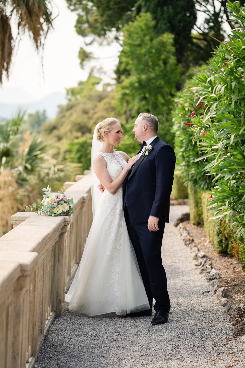 Wedding couple posing along a rustic stone wall pathway with tropical foliage.