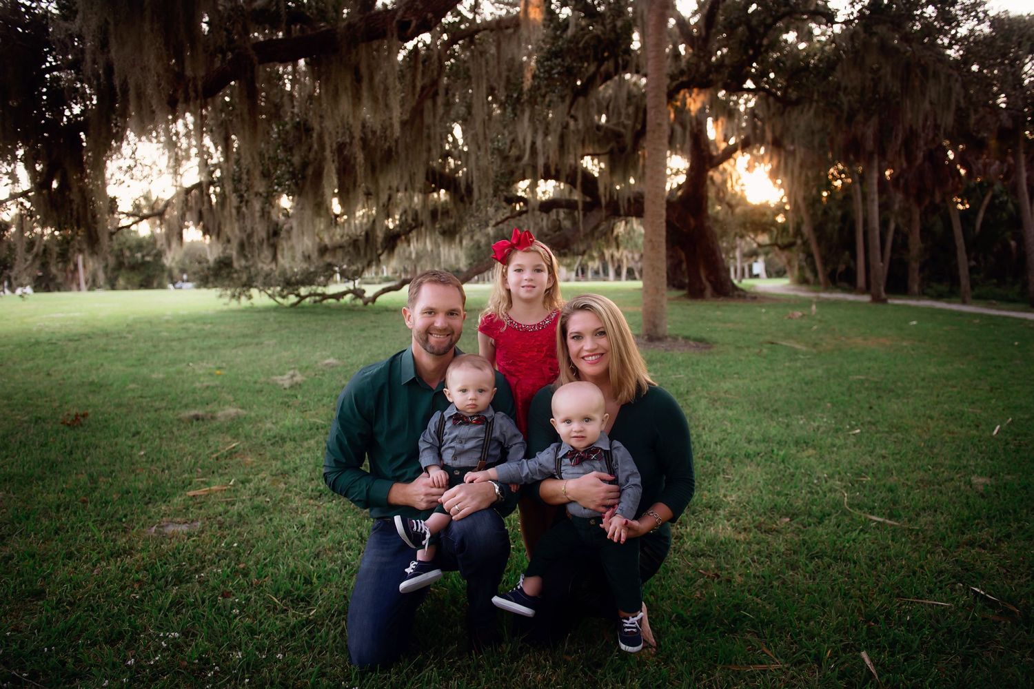 Spanish moss drapes over trees in a serene park setting at sunset.