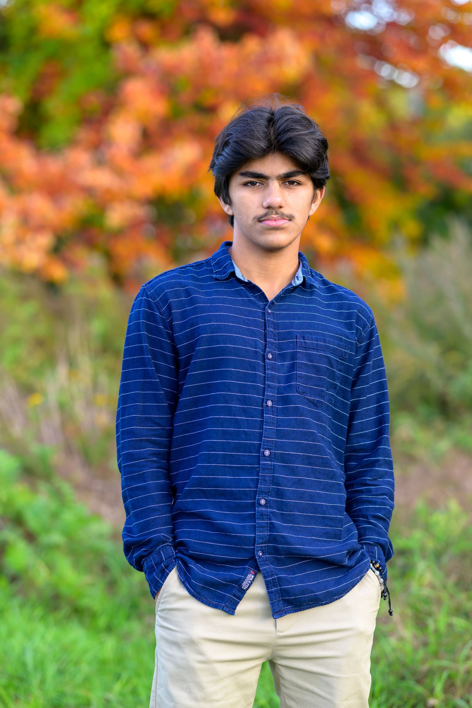 A young Indian man posing for his high school senior portrait in autumn.