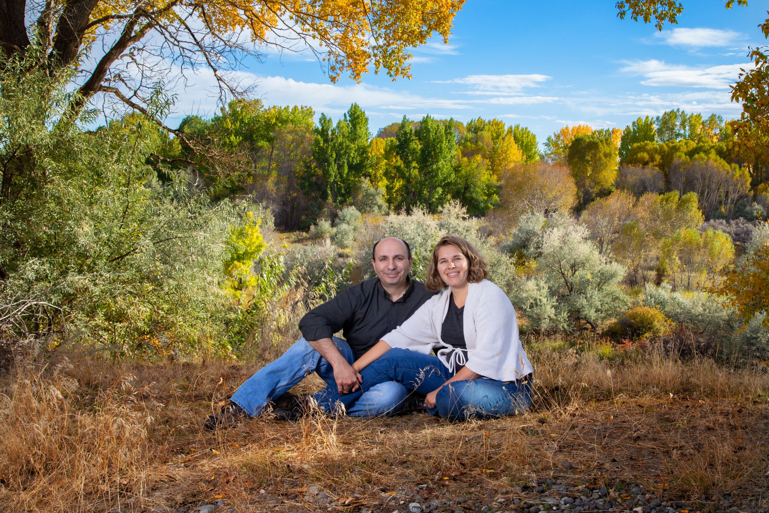 Couple sitting under fall foliage tree with golden autumn colors in background.