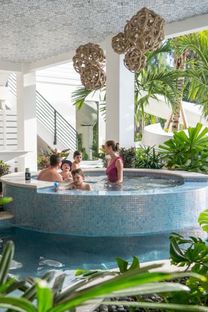 A family enjoys time together in a round mosaic hot tub surrounded by lush tropical greenery.