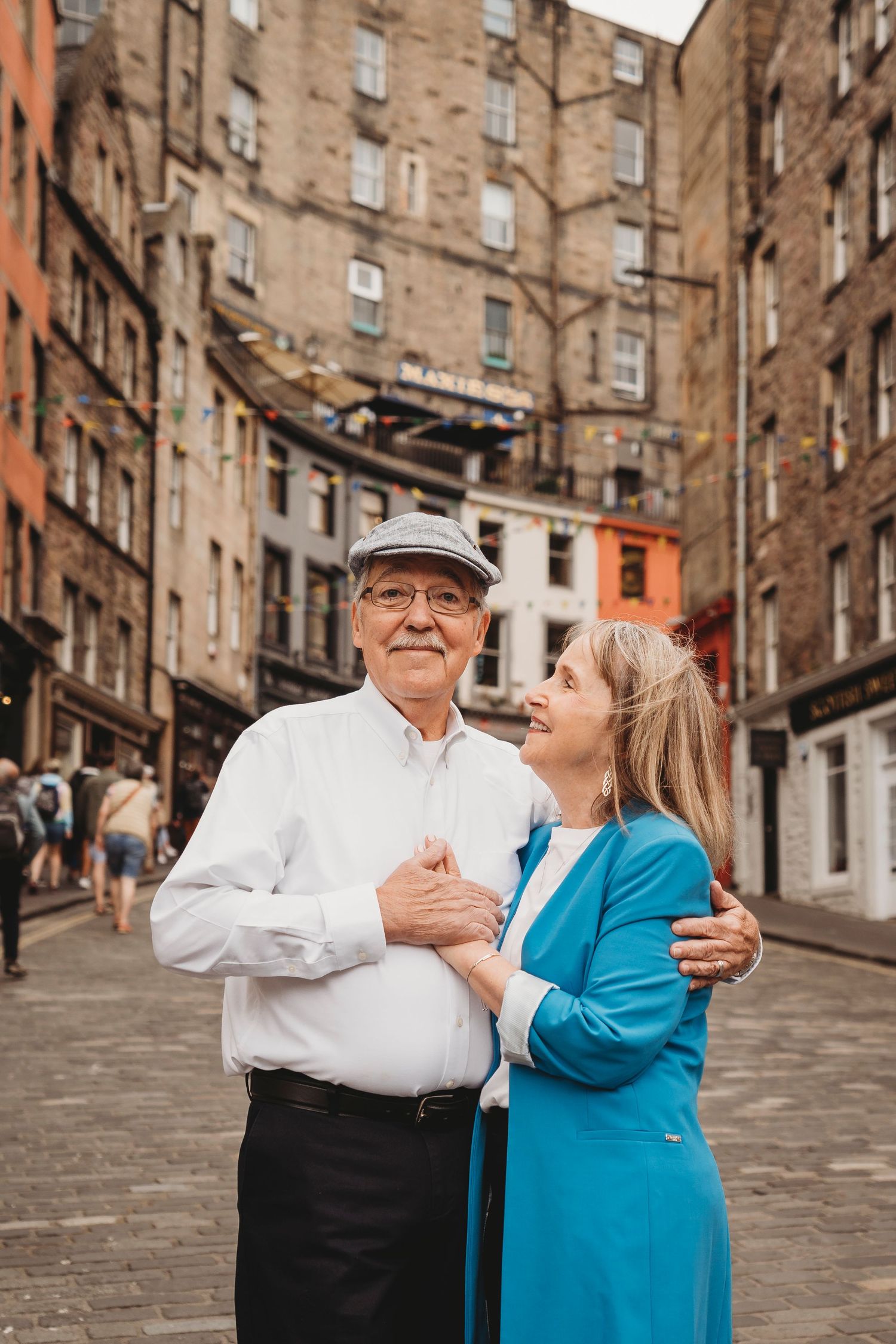 Elderly couple sharing tender moment on historic Edinburgh street.