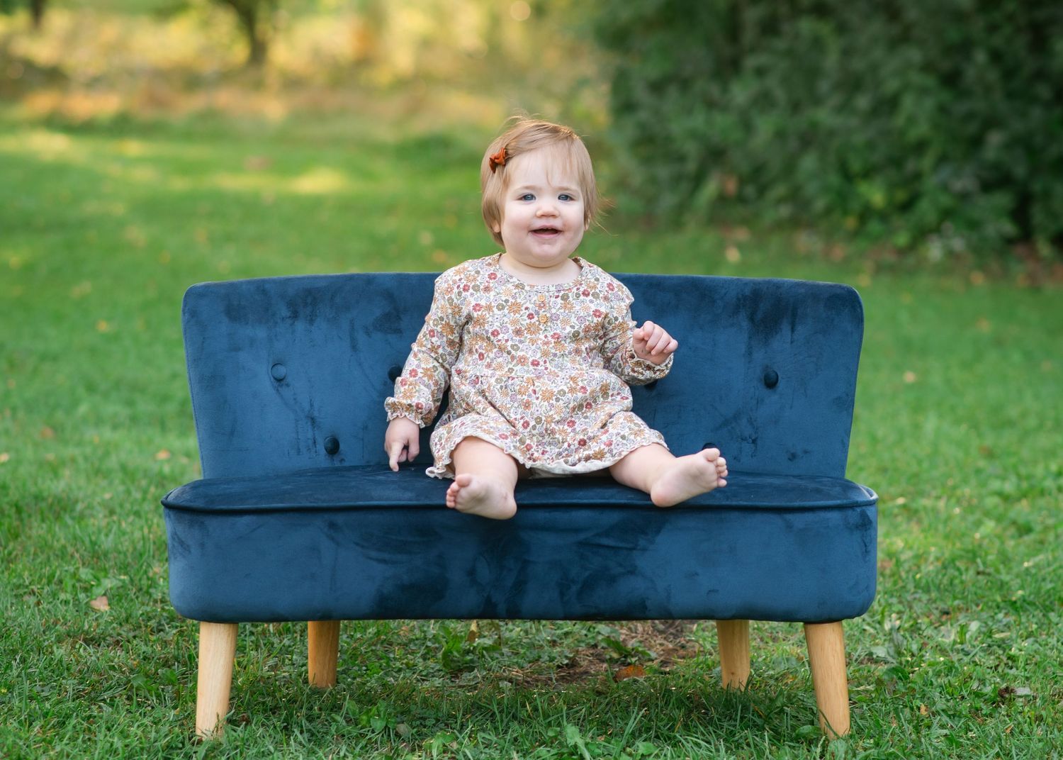 A vintage blue velvet loveseat sits on grass during an outdoor portrait session.