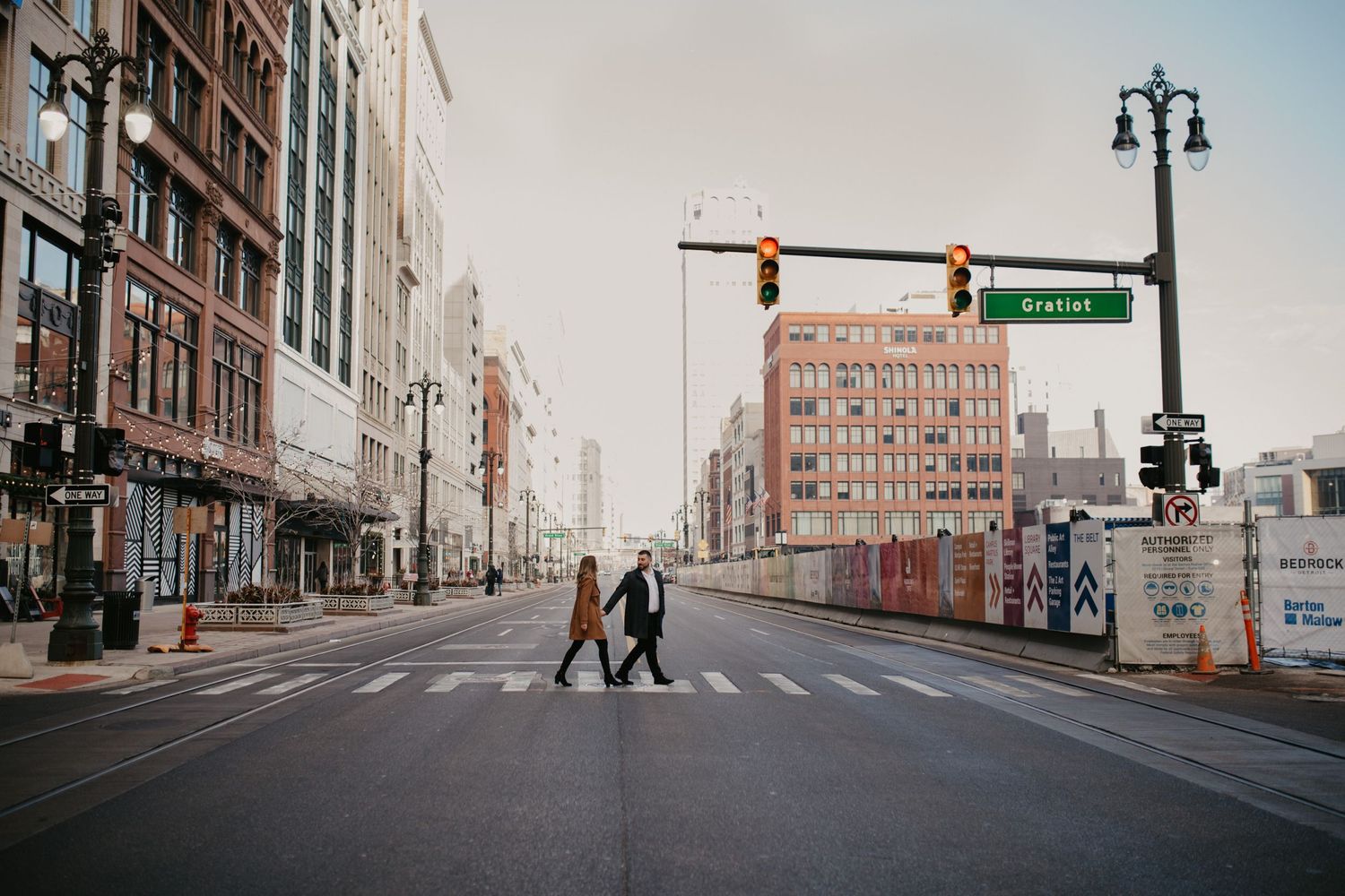 A couple walks across an empty urban street intersection with vintage buildings in the background.